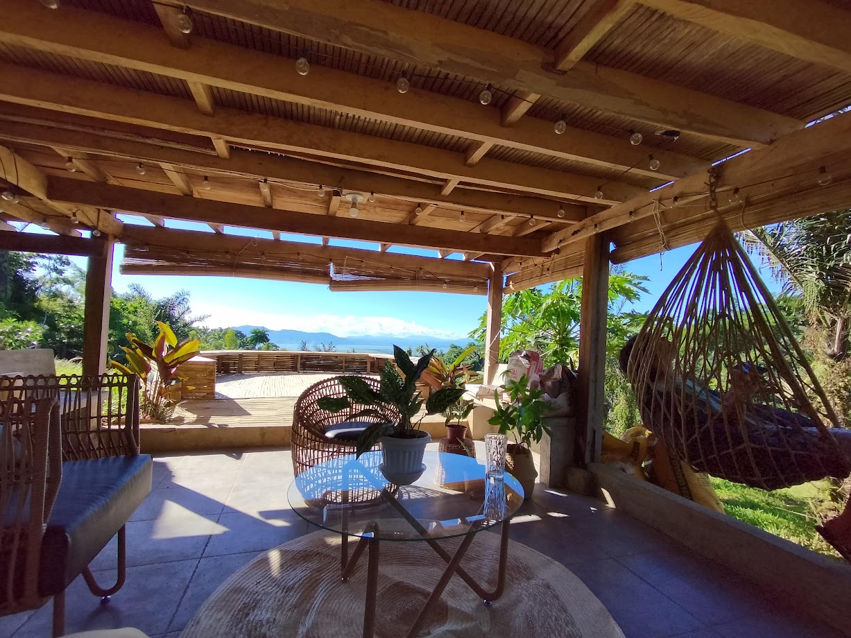 Tropical terrace lounge with rattan seating, hanging chair, glass coffee table, and panoramic bay views from a vacation rental